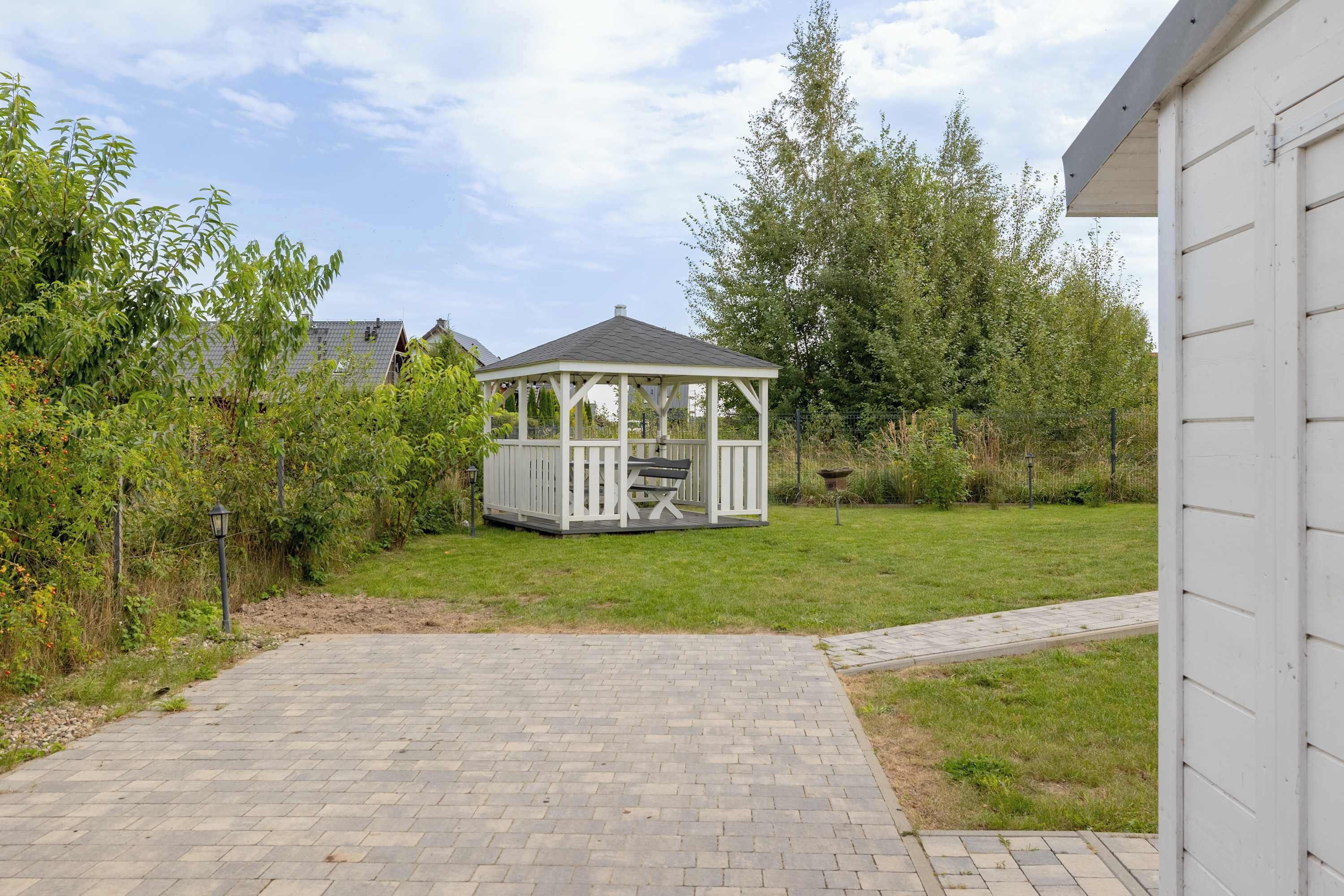 A gazebo with a bench in a backyard with a paved path leading to it.