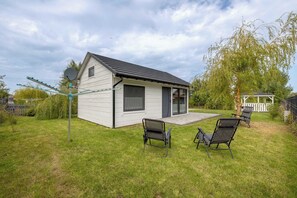 Ett litet, envåningshus med ett sluttande tak och en satellitantenn på vänster sida. Framför huset står två svarta trädgårdsstolar.