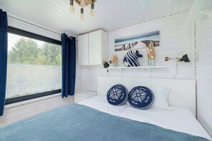 A bedroom with a large bed, a window with curtains, a white headboard, and a shelf with decorative items.