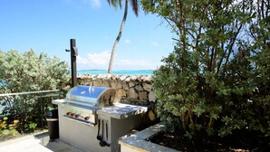 An outdoor grill area with a stone wall and a view of the ocean. - Two Bedroom Cable Beach Condo With Patio (Nassau)