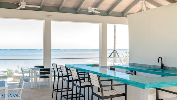 A modern kitchen with a large island, bar stools, and a view of the ocean. - Two Bedroom Cable Beach Condo With Patio (Nassau)