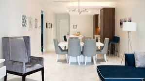 A modern living room with a dining area, featuring a grey upholstered armchair, a blue sofa, and a dining table with four grey chairs. - Two Bedroom Cable Beach Condo With Patio (Nassau)