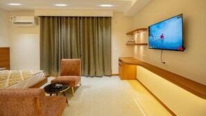 Ett hotellrum med en säng, två fåtöljer, ett litet bord, en tv som är monterad på väggen och en luftkonditioneringsanläggning.