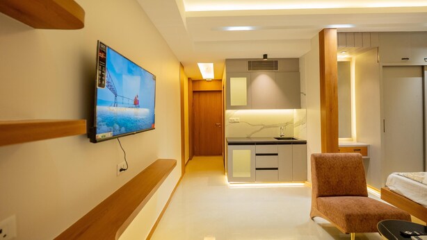 Ett modernt hotellrum med en TV som är monterad på väggen, en träbänk, en sittgrupp med en bekväm fåtölj, ett litet bord och en säng.