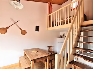 A wooden dining table with chairs, a wooden staircase, a ceiling light fixture, and a wall-mounted picture. - Holiday Home - 'La Maison Bleue' (La Tranche sur Mer)
