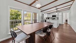 Una cocina amplia con vigas de madera, un comedor con una gran mesa y sillas, y vistas al exterior a través de grandes ventanales.