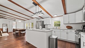 Una cocina moderna con armarios blancos, un refrigerador de acero inoxidable y una mesa de comedor de madera.