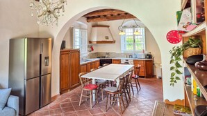 A kitchen with a central island, wooden cabinets, a stainless steel refrigerator, and a chandelier.