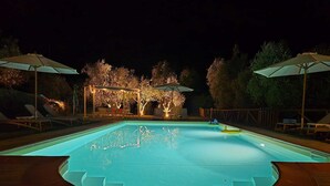 A swimming pool with a tiled deck, surrounded by lounge chairs and umbrellas.