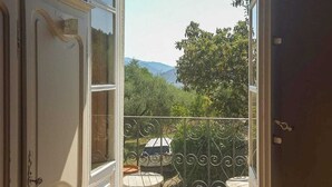 An open door leading to a balcony with a view of trees and mountains.