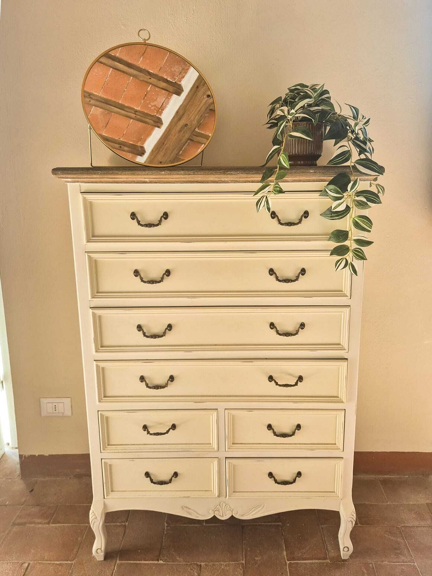 A cream-colored dresser with six drawers, a mirror, and a potted plant on top.