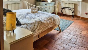 A bedroom with a bed, a dresser, a desk, and two windows with a view of greenery.