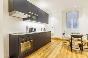 Una cocina moderna con armarios oscuros, horno empotrado y comedor con mesa y sillas redondas.