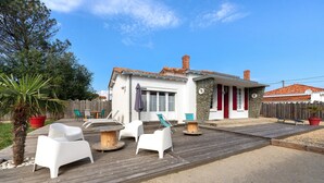 A house with a patio, white chairs, a wooden deck, and a stone wall.