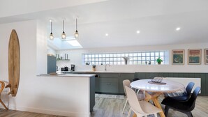 A modern kitchen with a central island, pendant lighting, and a dining area with chairs.