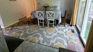A dining area with a table set for two, a ceiling fan, a painting on the wall, and a window with curtains.