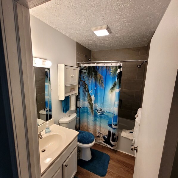 Un baño con cortina de ducha con motivos tropicales, un lavabo blanco y un inodoro.