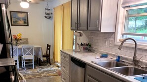 A kitchen with grey cabinets, a sink, and a window. There is a dining area with a table and chairs.