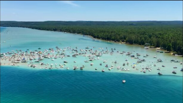 An aerial view of a coastal area with numerous boats and a small island with dense forestation.