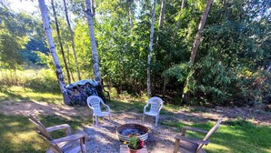 An outdoor seating area with a fire pit, two white plastic chairs, and a wooden bench.