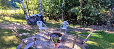 An outdoor seating area with a fire pit, two white plastic chairs, and a wooden bench.