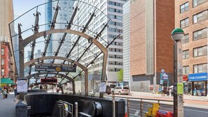 A subway station entrance with a modern glass canopy, a sign for 72 Street Subway Station, and a nearby ATM.