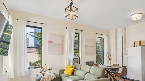 A modern living room with a green sofa, a small round table, and a dining area with a white refrigerator.