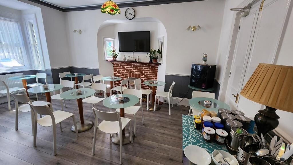 Un comedor con mesas redondas de cristal y sillas blancas, chimenea de ladrillo, televisor de pantalla plana y un reloj en la pared.