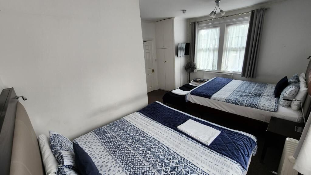 Ein Schlafzimmer mit zwei Betten, einem Fernseher, einem Fenster mit Vorhängen und einer Heizung.