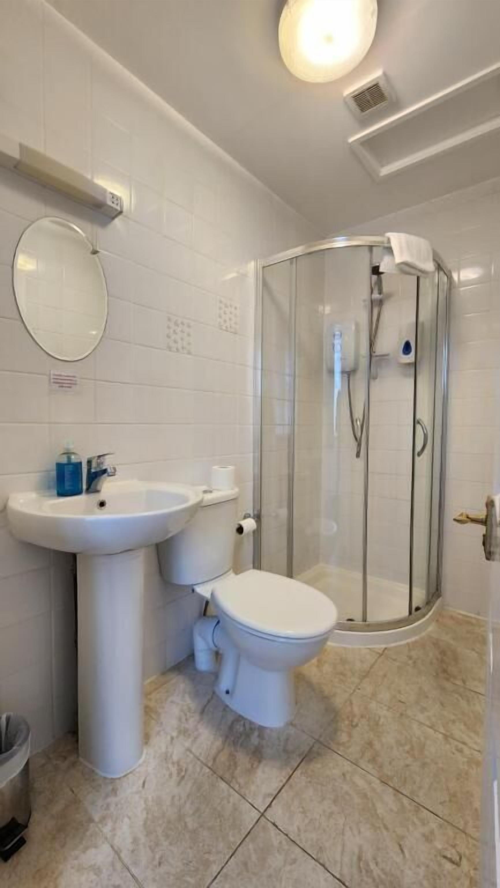 A modern bathroom with a glass-enclosed shower, a pedestal sink, and a toilet.