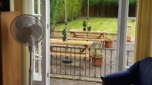 A room with a bed, a fan, and a view of an outdoor patio with a table, chairs, and an umbrella.