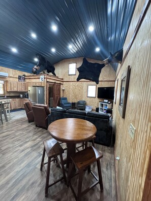 Un interior rústico con una mesa y sillas de madera, un sofá y una zona de cocina con refrigerador y alacenas.