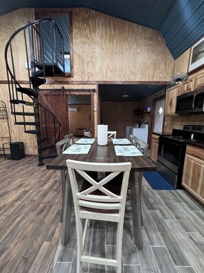 Cocina compacta con armarios de madera, un microondas y una estufa. Una escalera en espiral conduce a un nivel superior.