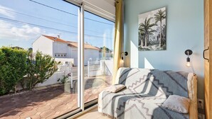 Ein Zimmer mit Bett, einem Bild, einem Fenster und Blick auf ein Haus und Bäume.