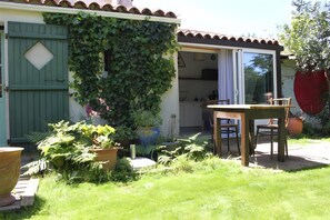 Een huis met een groene deur, een schuifdeur van glas naar een keuken, en een houten tafel met stoelen buiten.