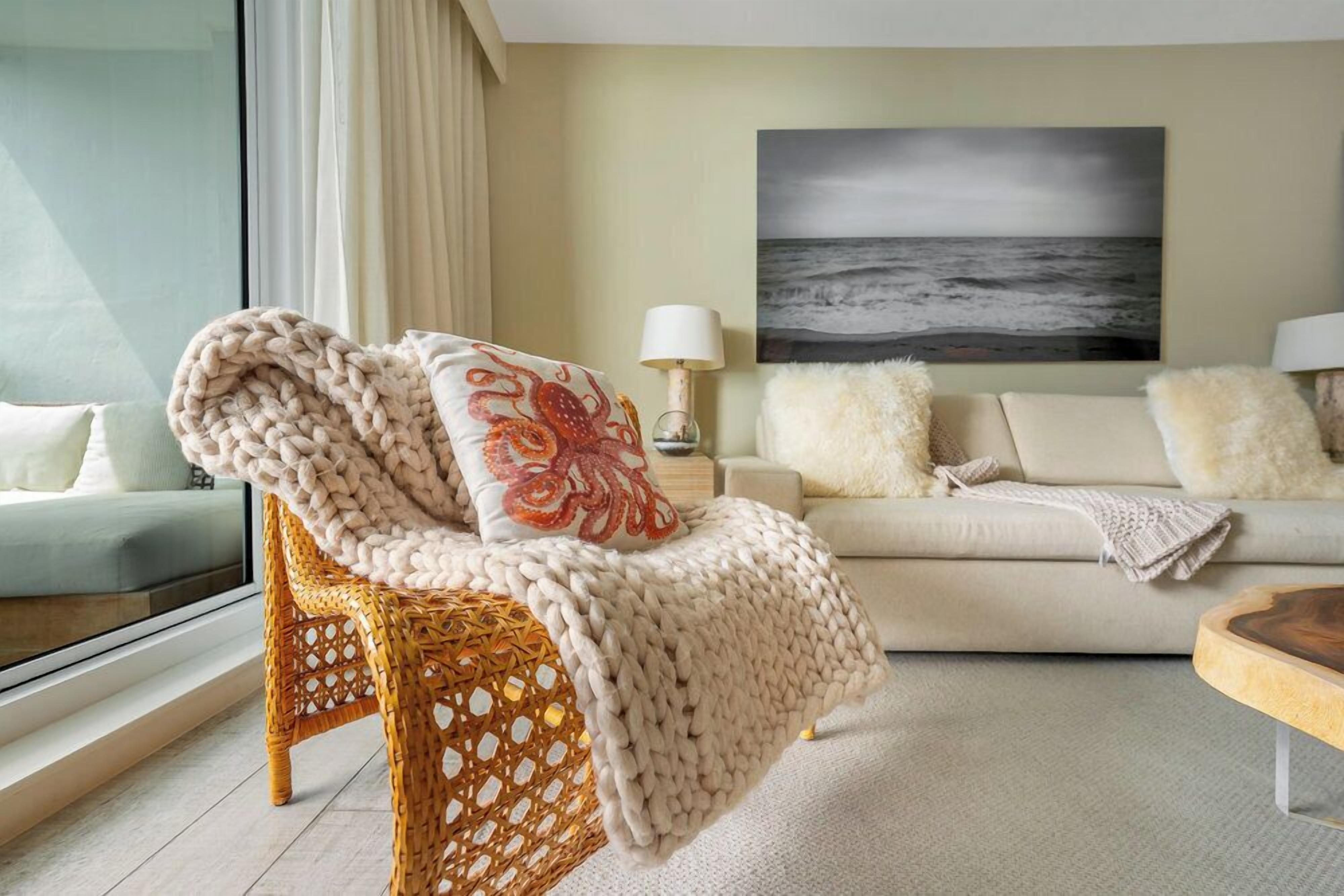 Un soggiorno accogliente con una poltrona in vimini, un divano e un quadro che raffigura l'oceano.