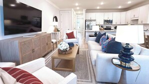 Een moderne woonkamer met een flatscreen televisie, een plafondventilator en een keuken op de achtergrond.