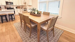 Een moderne keuken met witte kasten, een houten eettafel en een groot raam met zonwering.