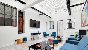 Una sala de estar moderna con un sofá azul, una mesa de centro y una estatua de Buda. Hay dos sillones azules, una mesita y un televisor montado en la pared.