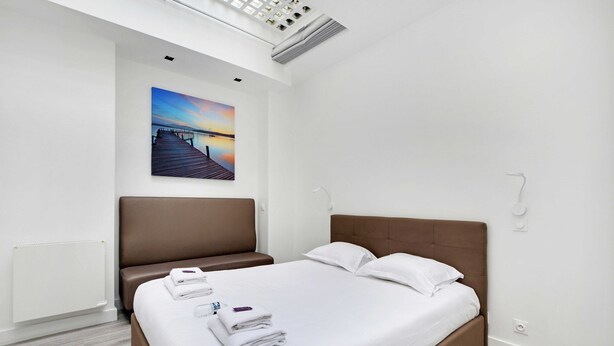 Habitación de hotel moderna con una cama grande, cabecera marrón y vista al atardecer sobre un muelle.