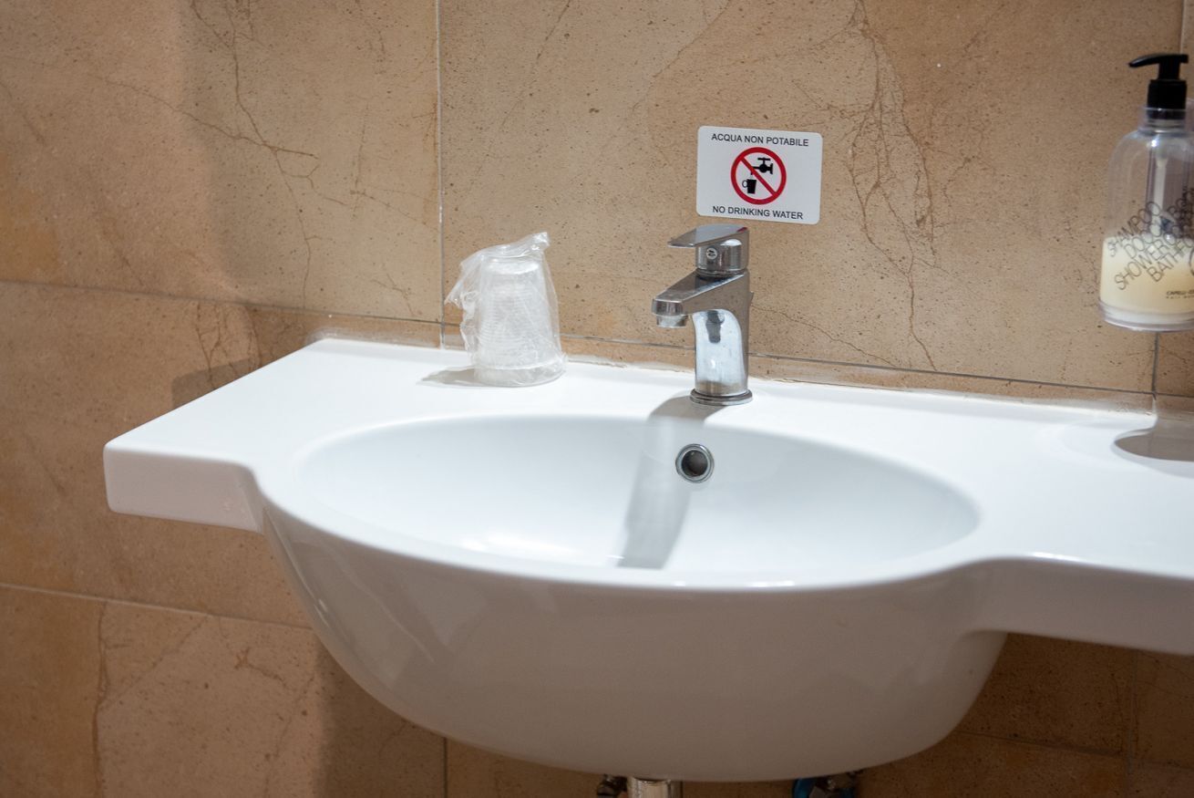 Een wastafel in een badkamer met een bordje 'Geen Drinkwater', een zeepdispenser en een plastic zak.