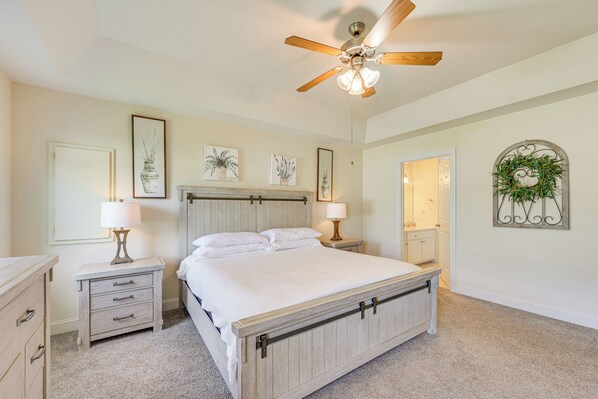A bedroom with a wooden bed, two bedside tables with lamps, a ceiling fan, and framed botanical prints on the walls.