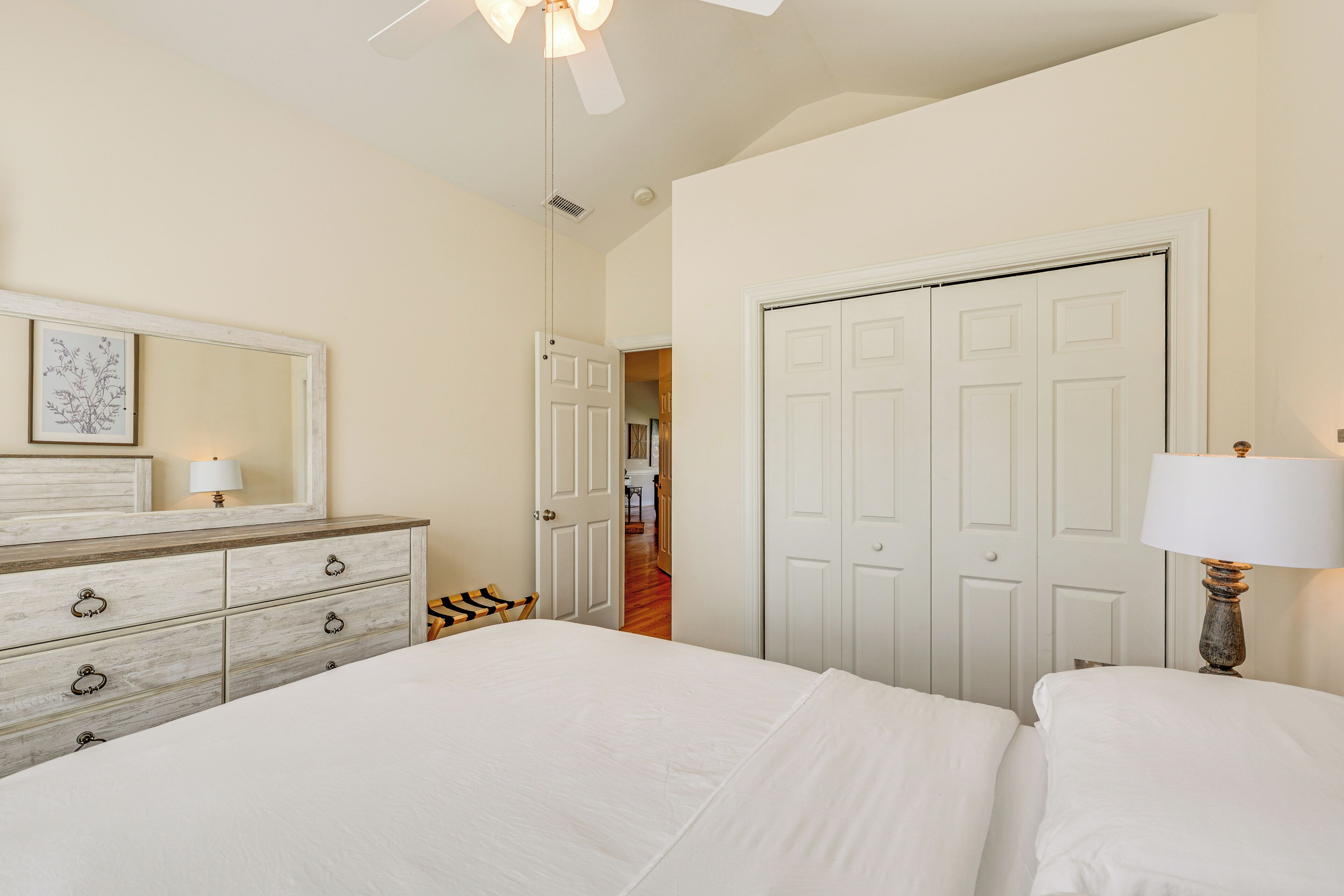 A bedroom with a bed, dresser, and a door leading to another room.