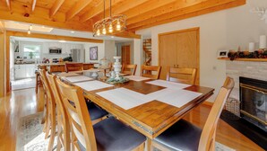 A spacious dining area with a wooden table and chairs, a chandelier, and a fireplace. - Ski, Hike & Game: White Mountains Family Retreat (Campton)