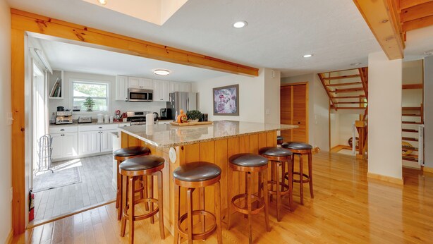 A spacious kitchen with white cabinets, a central island with stools, and a wooden ceiling. - Ski, Hike & Game: White Mountains Family Retreat (Campton)