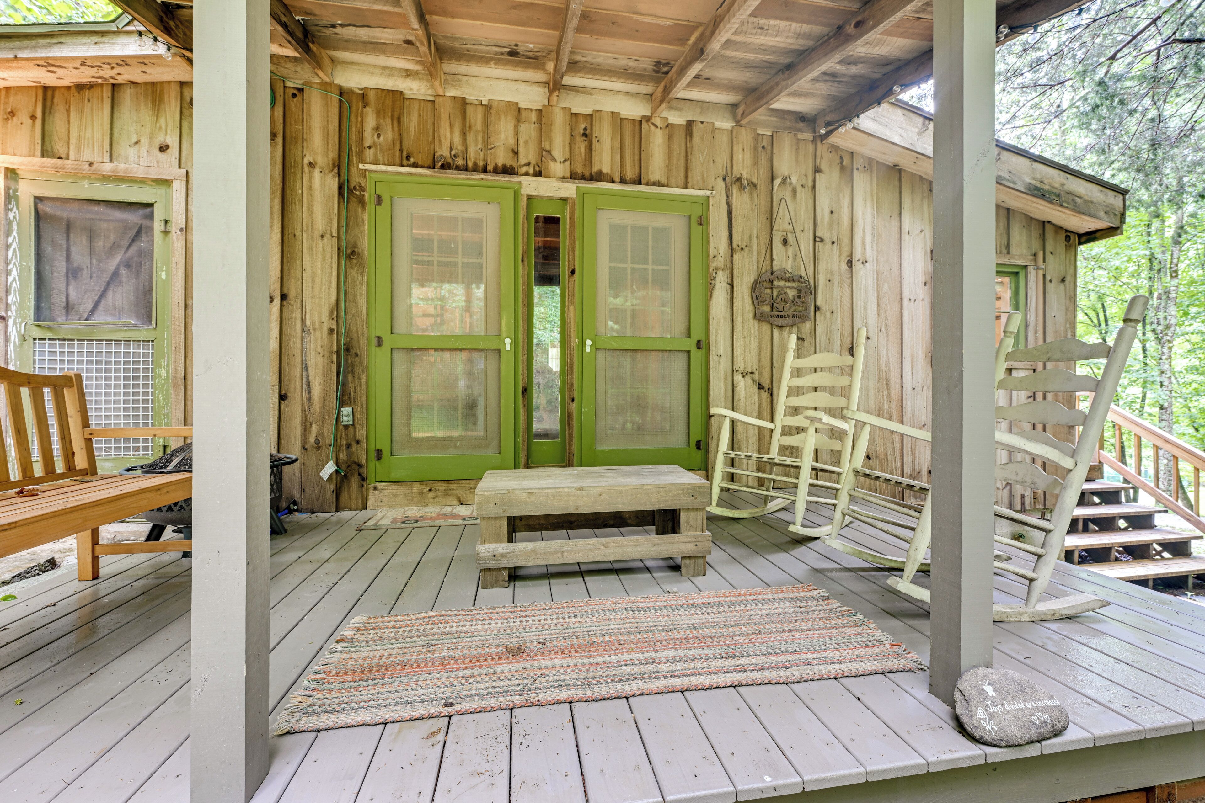 Een houten chalet met een veranda, een bank, een schommelstoel en een trap die naar een verdieping leidt.