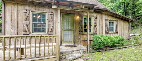 A rustic wooden cabin with a porch, a stone entrance, and a small garden area.