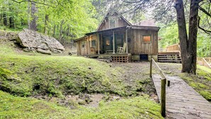 A rustic cabin with a porch, surrounded by lush greenery and a wooden deck leading to the entrance. - Trail Access & Tranquil Setting: Franklin Retreat! (Franklin)
