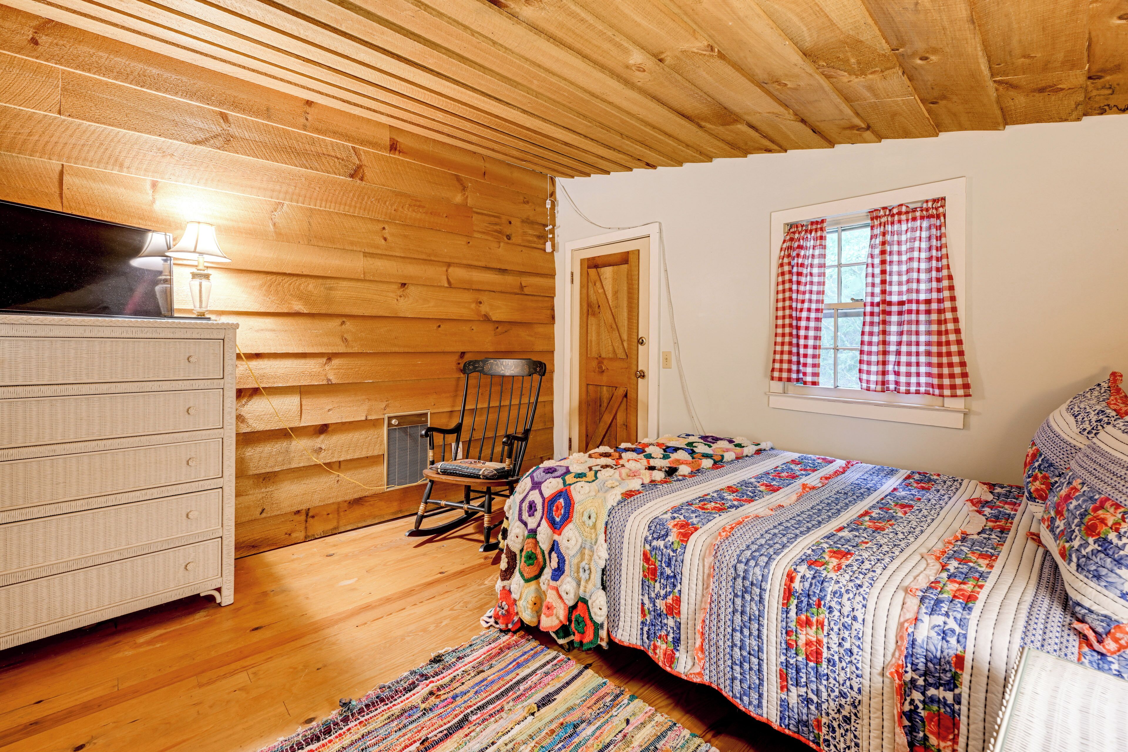 A cozy room with wooden walls, a bed with a colorful quilt, a dresser, and a rocking chair.