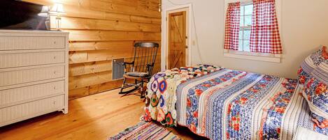 A cozy room with wooden walls, a bed with a colorful quilt, a dresser, and a rocking chair.